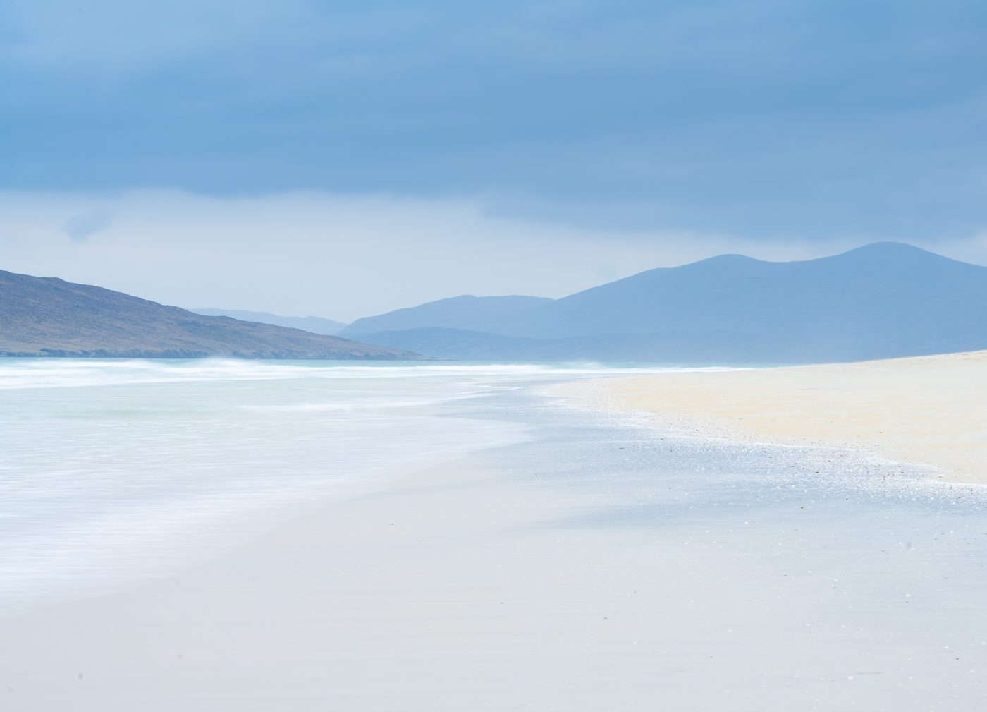 Pale sandy beach beneath blue mountains on Harris